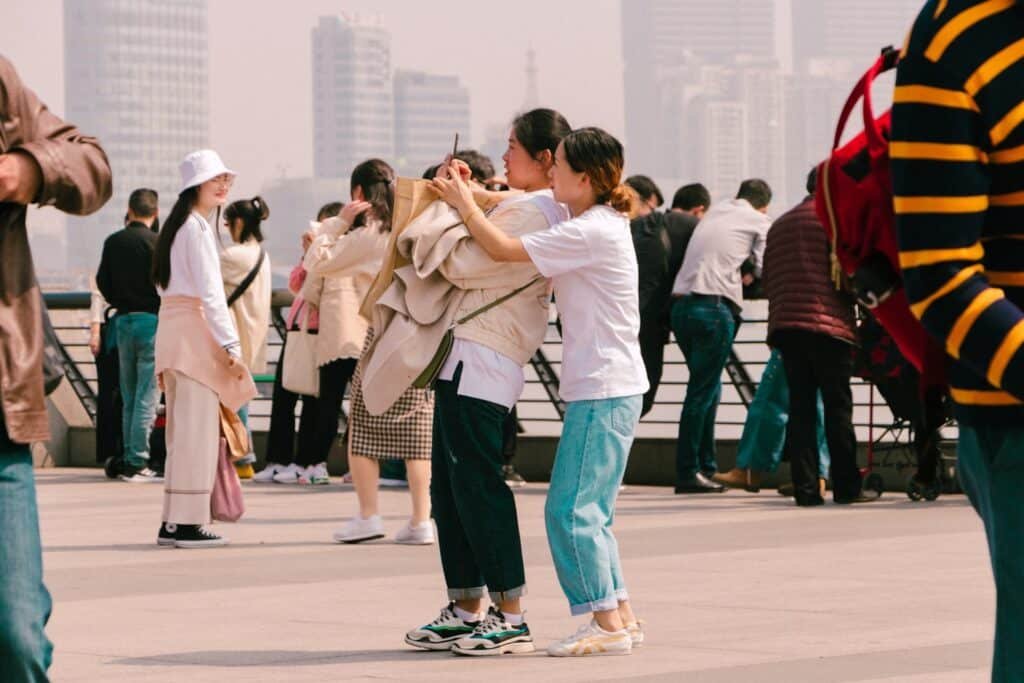 Duas mulheres tirando uma foto juntas em um calçadão da cidade com pessoas e prédios altos ao fundo. Ilustra o eSIM Xangai.