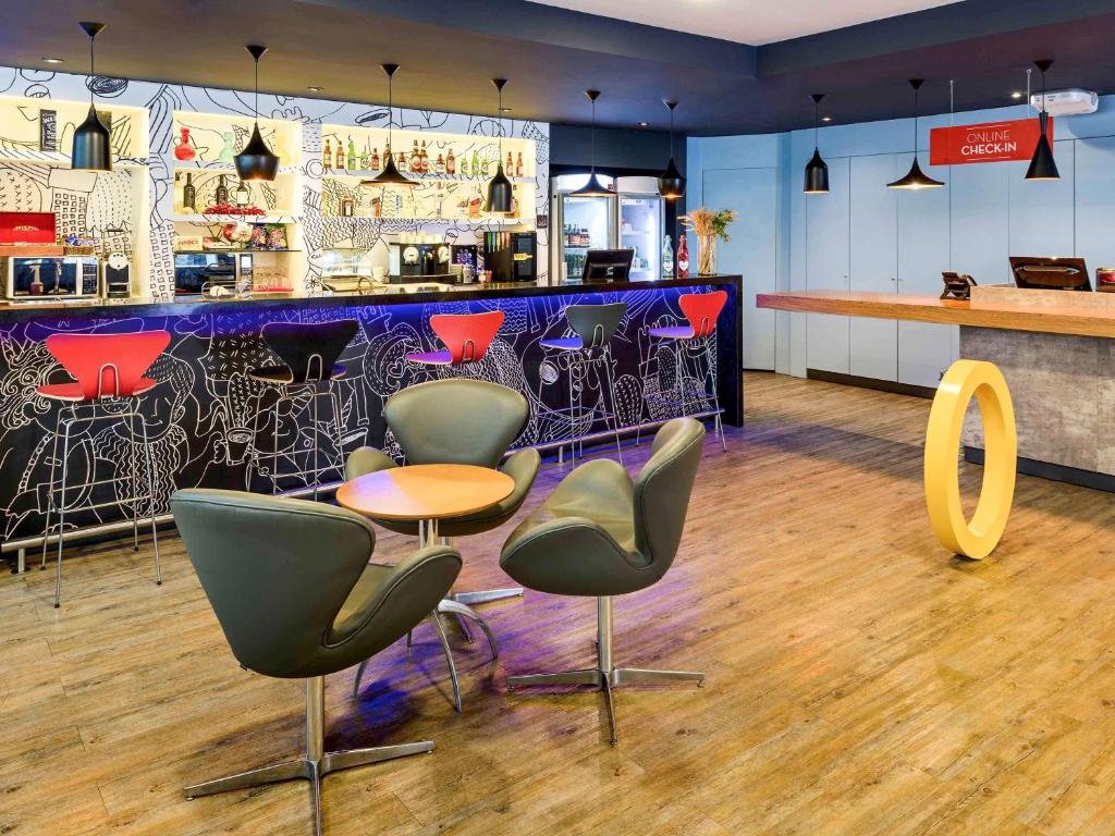 Recepção do ibis santos dumont nos hotéis do rio de janeiro, com decoração colorida, mesinha com poltronas, banquetas no balcão e área de refeições ao fundo