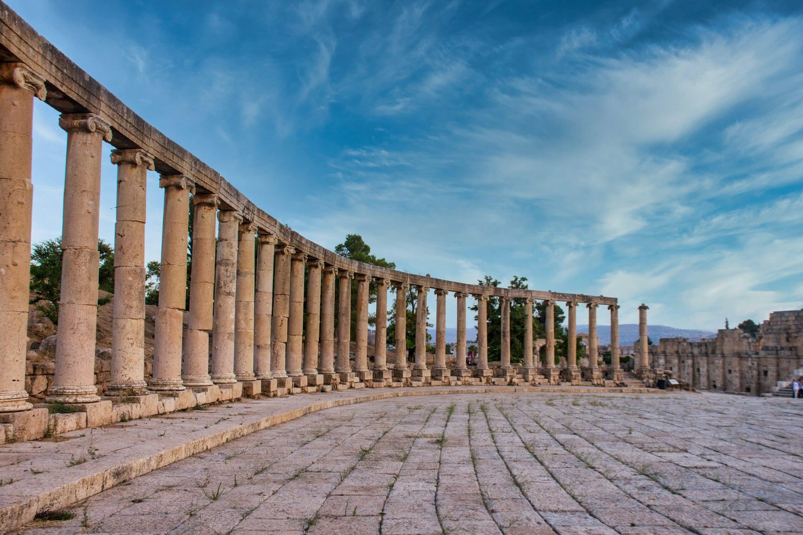 As ruínas em Jerash, na Jordânia, durante o dia com arcos e colunas, no estilo greco-romano com árvores ao fundo.
